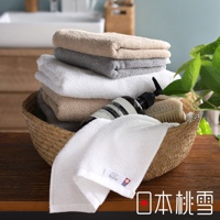 一籃中堆疊著淺棕色、灰色和白色的今治毛巾，毛巾質地輕薄柔軟。籃中另有黑色瓶裝洗手乳和木質毛刷。