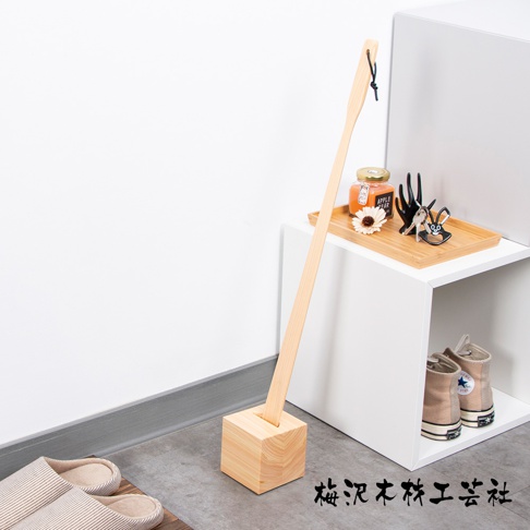 加長檜木鞋拔，木質鞋拔本體呈淺木色，末端有黑色繫繩，底部為方形木座，整體設計簡約。