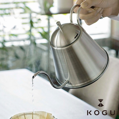 手持一只日本製18-8不鏽鋼極細口咖啡手沖壺，壺身呈現銀色金屬光澤，壺嘴細長，正緩慢傾倒出水，壺蓋頂部有細長的出氣孔。