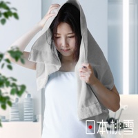 一位女性頭上蓋著一條淺灰色的厚手迷你浴巾，雙手將浴巾固定在頭部。浴巾材質可見細緻的紋理。