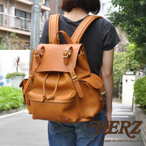 職人手作棕色皮革復古風旅行後背包，採用抽繩閉合設計，搭配多個帶有金屬扣的翻蓋口袋，適合日常或旅行使用。