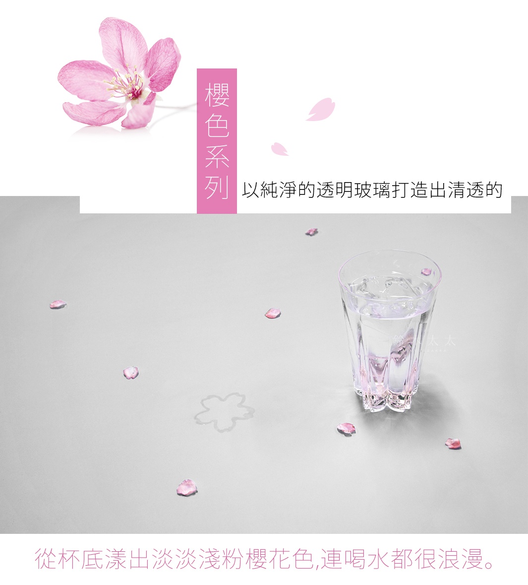 透明玻璃清酒杯，底部帶有淡淡的粉色櫻花圖案，杯中盛有冰塊和透明液體，周圍散落著幾片粉色櫻花花瓣。