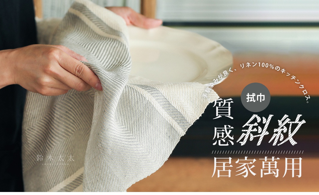 一雙手拿著一塊米白色亞麻斜紋編織的廚房拭巾，上面有細緻的灰白色條紋。