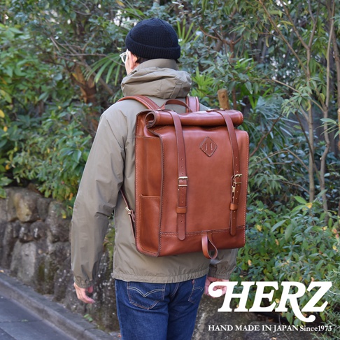棕色皮革製成的大容量後背包，採用捲蓋設計，配有可調節的肩帶和側邊口袋，適合戶外活動。