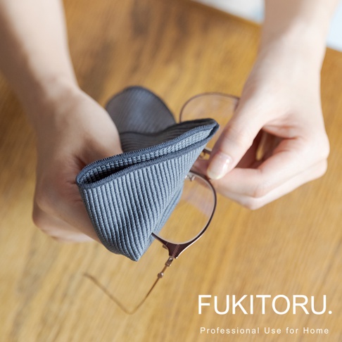 雙手正用一塊深灰色、有細緻條紋紋理的超極細纖維清潔布擦拭一副玫瑰金金屬框眼鏡。