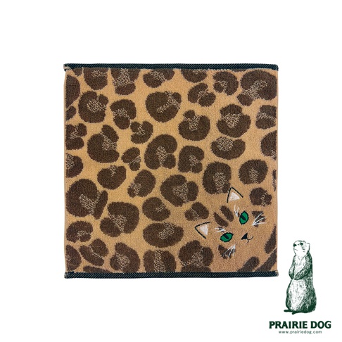 一張方形的 Prairie Dog 品牌今治毛巾，底色為溫暖的淺棕色，印有深棕色的豹紋圖案。毛巾右下角刺繡著一隻貓咪的局部臉部，擁有翠綠色的眼睛、精緻的白色鬍鬚與尖耳朵，與豹紋背景巧妙融合。右下角標註有 Prairie Dog 品牌名稱及其官方網站網址。