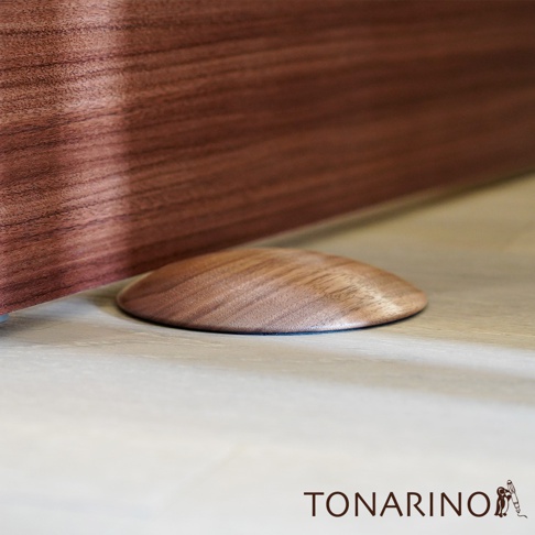 淺木紋地板上放置著一個圓潤的胡桃木色實木門擋，門擋表面有自然的木紋紋理。