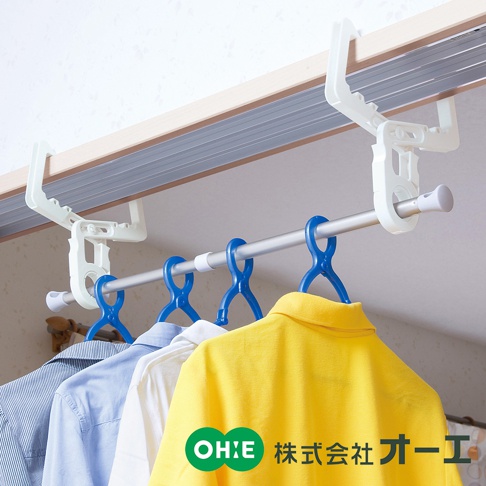 白色塑膠門樑晾掛組，由兩個可調節的白色支架固定於門框上方，懸掛著一根銀色金屬桿，桿上掛有數個藍色塑膠衣架，架上晾掛著條紋襯衫、白色襯衫及黃色 Polo 衫。