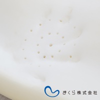 白色護頸止鼾枕，表面佈滿大小不一的透氣孔，材質呈現柔軟的記憶棉質地，中央有藍色曲線標誌與日文公司名稱「まくら株式会社」。