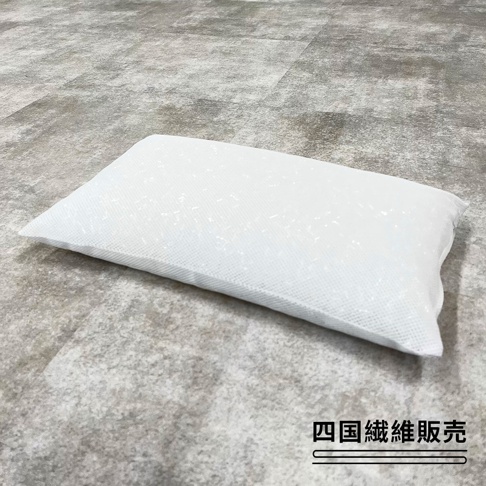 一個白色長方形的四國纖維便攜枕頭平放在灰色紋理的地板上，枕頭表面呈現細緻的網狀編織質感，右下角標註有四國纖維販賣的文字。