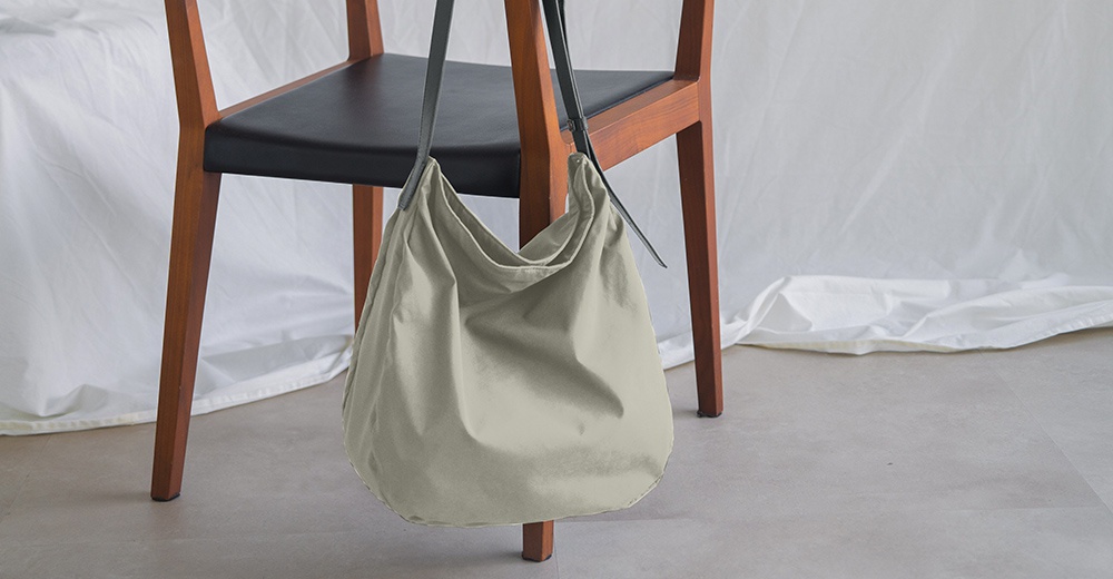Atelier nuu ssent 肩背托特包，簡約卡其色帆布材質，懸掛在木質座椅上。