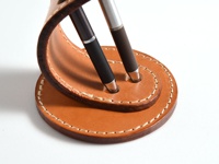 職人手作皮革兩入用筆架，淺棕色皮革，搭配米白色縫線，可容納兩支筆，設計簡約。