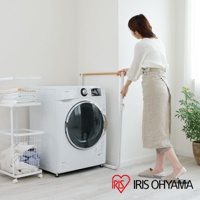 簡約白色金屬框架搭配原木橫桿的曬衣架，旁有滾筒式洗衣機與白色置物架，架上與下方籃筐內有衣物，一位女性穿著亞麻圍裙站在曬衣架旁。