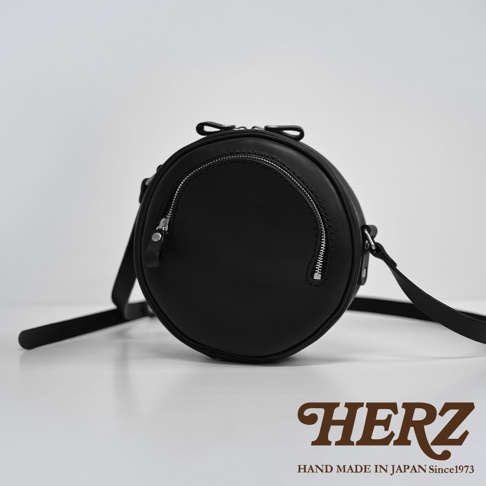 黑色皮革製成的小圓包，包身圓潤，正面設有拉鍊隔層，搭配銀色拉鍊和皮革拉頭。