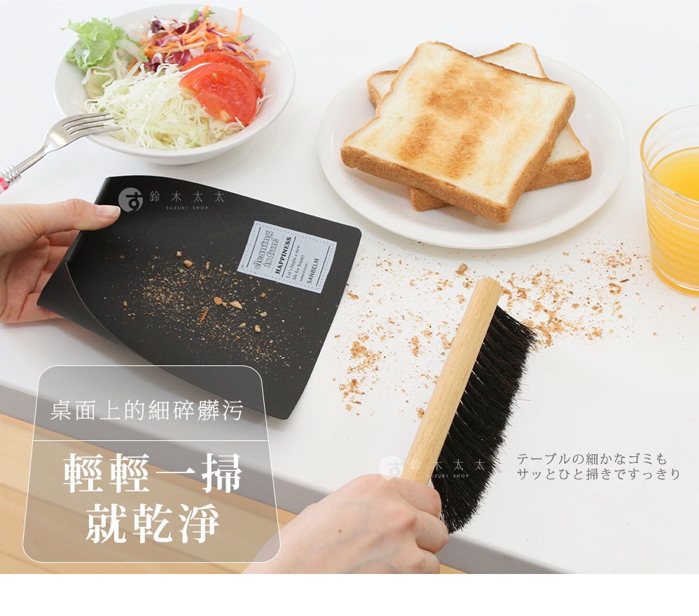 一隻手拿著黑色輕便畚箕，另一隻手持木柄黑色刷毛的小掃把，正在清理餐桌上的吐司麵包屑，背景為擺放早餐的餐桌，畫面呈現簡潔清潔的意象，帶有日式生活風格的桌面清掃工具組。