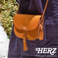 職人手作皮革流蘇側背包 CP-18，採用天然鞣製的淺棕色皮革，設有獨特的竹節鎖扣及皮革流蘇裝飾，搭配同色系皮革肩帶，整體呈現經典復古風格。