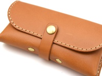 棕色皮革眼鏡收納盒，附有金屬按扣和手工縫線細節。