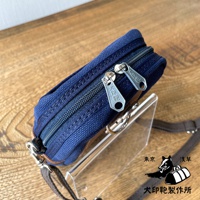 石洗帆布斜背手機包，深藍色，設有兩個拉鍊開口，銀色拉鍊上有「犬印」字樣。包包側面有咖啡色皮革飾邊，配有可拆卸的深棕色織帶。