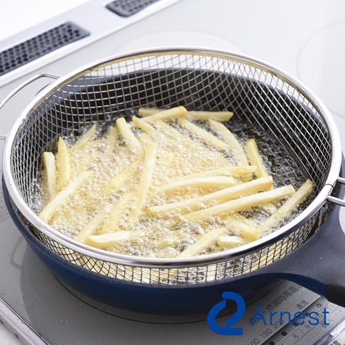 一個銀色不鏽鋼手持料理濾網，裡面裝滿正在油炸的薯條，薯條金黃酥脆，油鍋冒著泡泡，濾網放在一個藍色鍋子裡，鍋子放在爐台上。