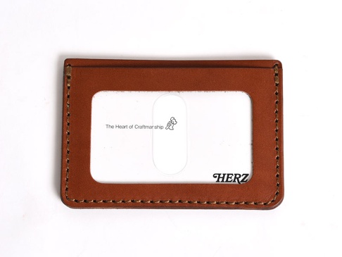 棕色皮革製成的橫式票券收納夾，有透明視窗，縫線精緻，右下方有「HERZ」品牌標誌。