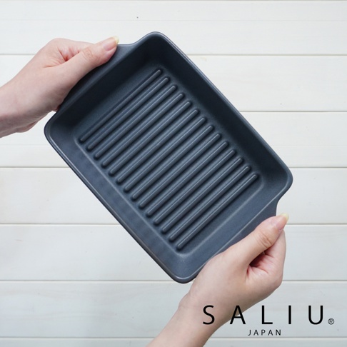 一隻手捧著深灰色、帶有條紋的長方形陶製烤盤，烤盤有兩個小提把，材質為耐熱陶瓷。