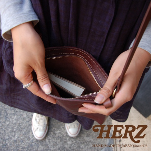 職人手作皮革Organ肩背小方包，深棕色，拉鍊開合，內有書籍，搭配同色系細長肩帶，展示包款的側面和內部細節。