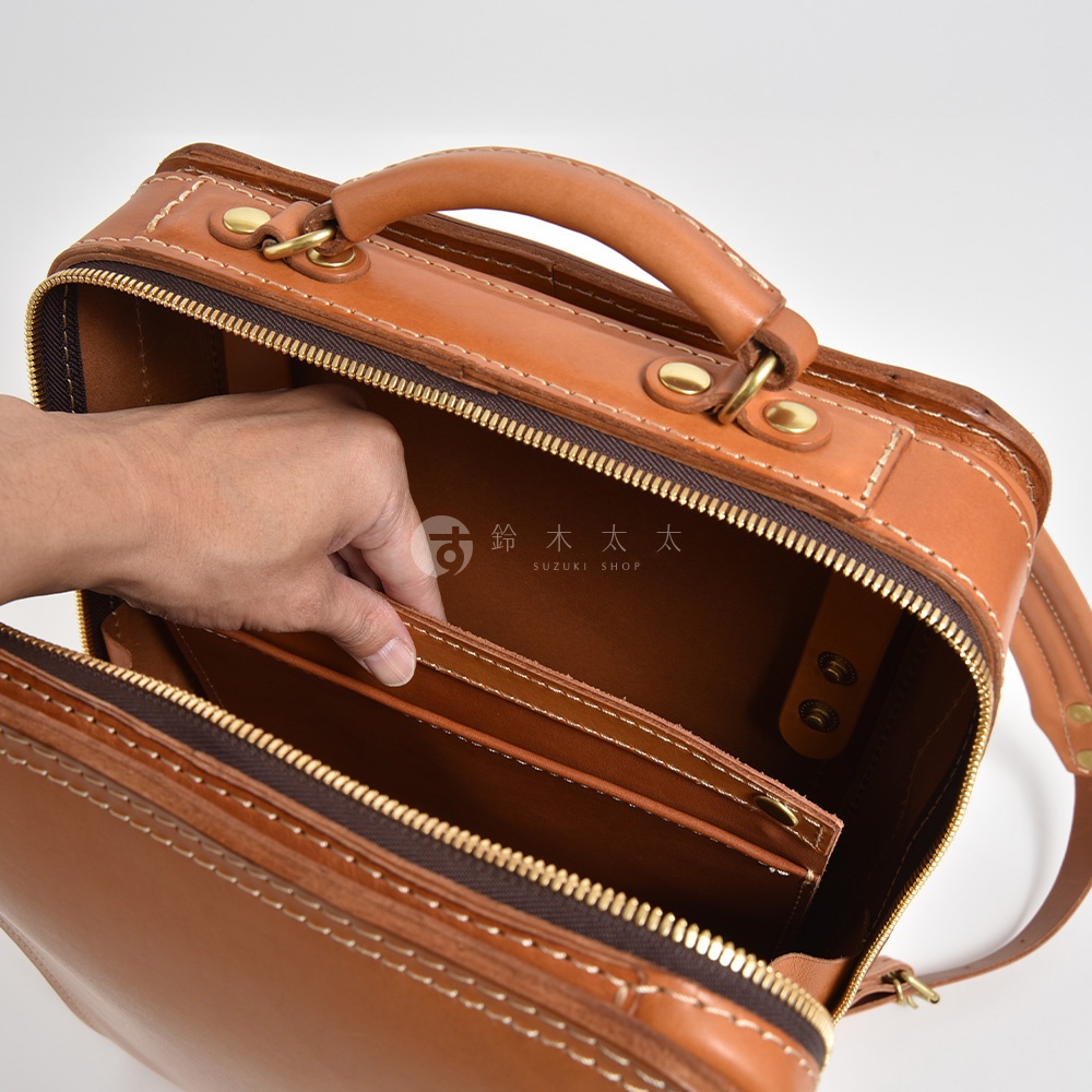 職人手作皮革商務電腦後背包 R-25，展示駝色款式，以頭層牛皮製成，包款採方形設計，設有頂部提把、雙向拉鍊開口，內部有分隔層，搭配金色五金配件與車縫線。
