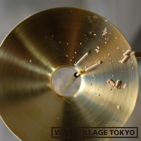 圓形黃銅線香架，帶有中心圓孔，架上散落著燃燒過的線香殘餘與灰燼。