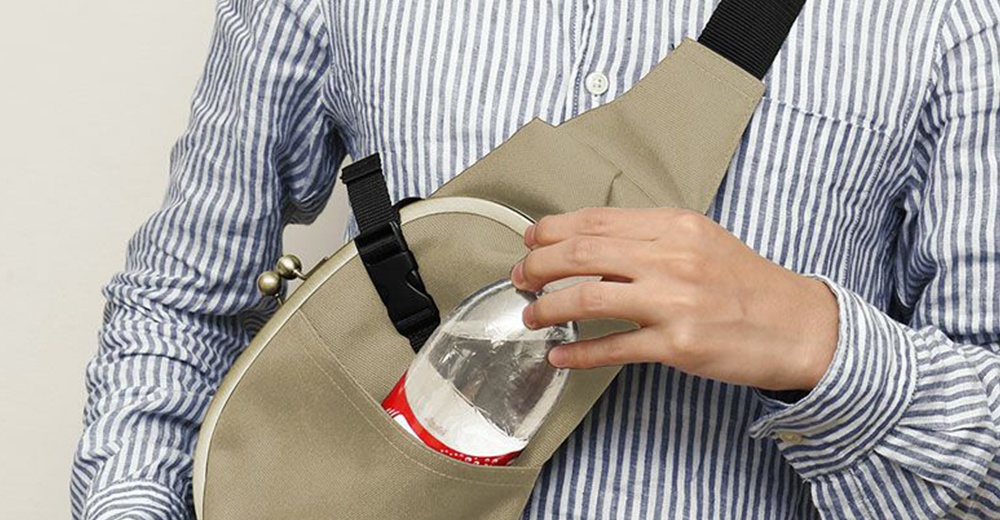 斜背包上有一個水滴形狀的口金，一位女士正將一瓶飲料放入背包的側袋中，她身穿條紋襯衫。