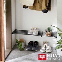 黑桿獨立腳伸縮層架，上面擺放著兩雙白色帆布鞋，右側有網狀籃子裝飾綠色植物。下方地面上擺放著兩雙運動鞋，左側也有盆栽裝飾。