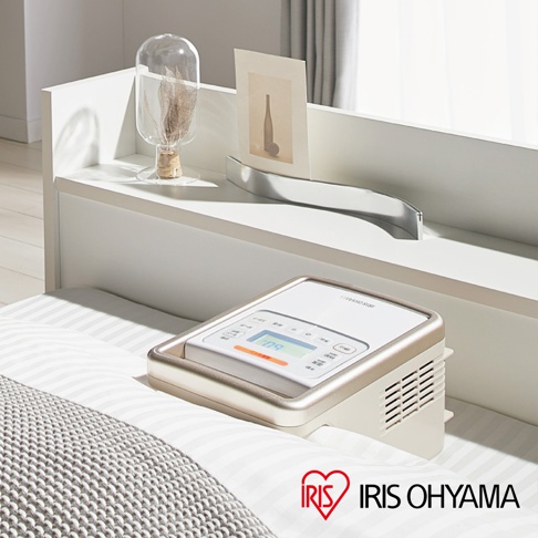 白色與金屬色調的強力被褥乾燥機 KFK301 放置在鋪有條紋床單的床上，機器上方有顯示螢幕與按鈕，側邊有散熱孔，整體呈現簡約現代風格。