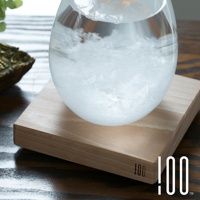 透明玻璃製成的 Tempo Drop 天氣瓶，內部充滿細緻的白色結晶，底部放置於淺木色木製底座上，呈現簡約自然的風格。