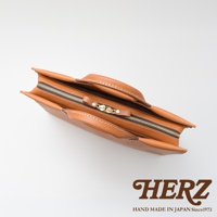 日本HERZ職人手作皮革公事包，頂部特寫，展現皮革的自然紋理與精緻縫線，搭配黃銅色拉鍊與提把，下方印有HERZ品牌Logo與「HAND MADE IN JAPAN Since1973」字樣。