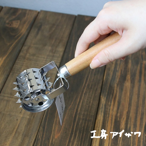手持不鏽鋼滾輪斷筋器，其滾輪部分由多個尖刺狀的不鏽鋼片組成，連接木質手柄。