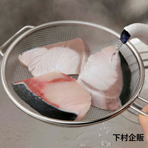 不鏽鋼淺型濾網裝著三塊生魚片，水從濾網上方流下，魚片呈現粉白色，帶有紅色魚肉紋理和黑色魚皮。