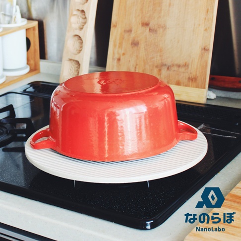 圓形珪藻土置物墊，白色底搭配細緻的灰色條紋，上方放置一個紅色圓形鑄鐵鍋。