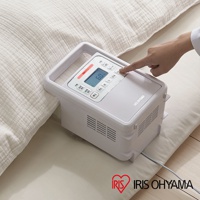 白色IRIS OHYAMA強力被褥乾燥機 FK-H1，配備LCD顯示屏和多個操作按鈕，側面有散熱孔，頂部有提把，置於米白色被褥旁。