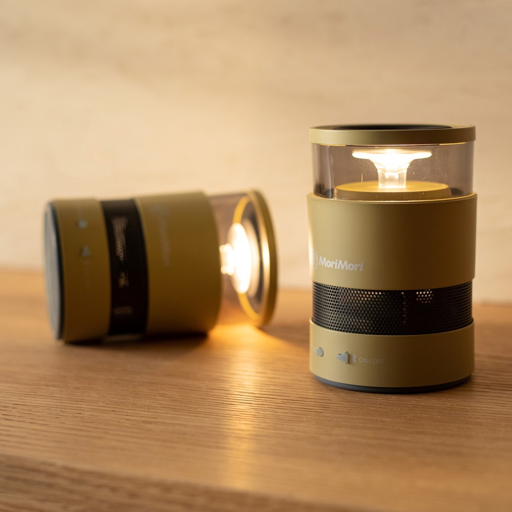 兩支黃褐色圓柱形氛圍燈音響，其中一支平放在木質表面，另一支直立，頂部發出溫暖的 LED 光，底部有網狀格柵和品牌標誌。