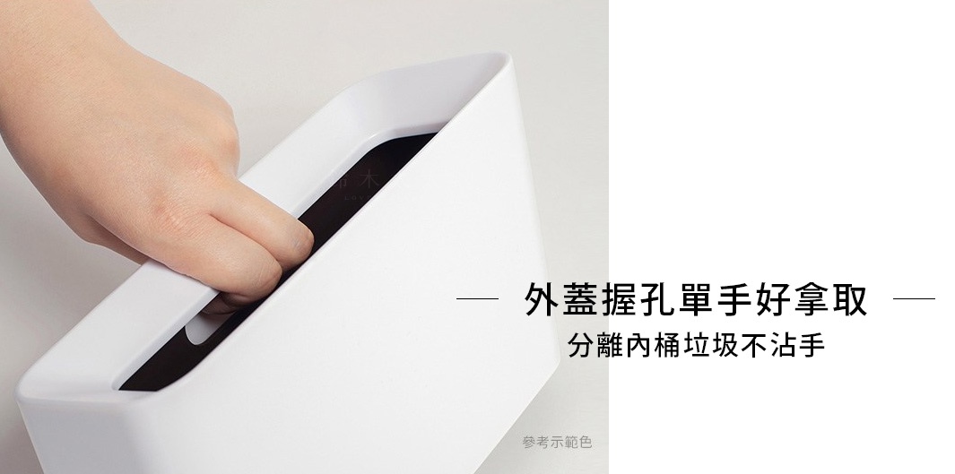 一張白色纖維板材質、斜口設計的桌邊置物/垃圾桶，內嵌黑色內桶，一隻手正在從置物槽中取出物品。