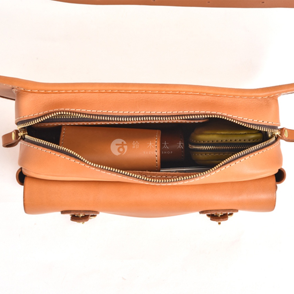 棕褐色皮革斜背包，拉鍊打開，內有咖啡色皮革長夾和綠色小圓包。
