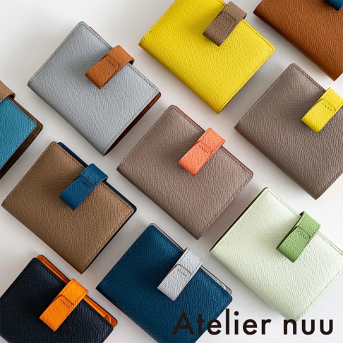 Atelier nuu 品牌的多種顏色皮革雙折短夾，包含灰色、黃色、橘色、淺綠色、藍色、棕色及黑色，皆帶有對比色的皮帶扣。