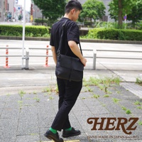 一名男子背著黑色的HERZ皮革馬鞍包，走在街道上。