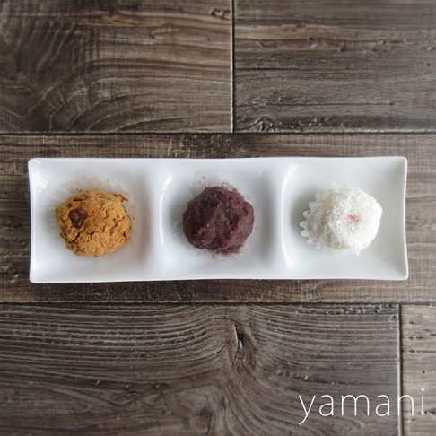 白色三格小菜盤盛放著三款日式和菓子，左邊是裹著黃褐色粉末的，中間是紅豆泥餡的，右邊是雪白糖霜外層的。