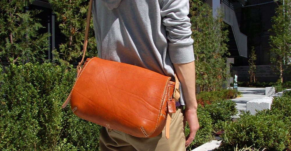 棕色皮革製郵差包，配有扣環和縫線細節，肩帶由皮革製成。