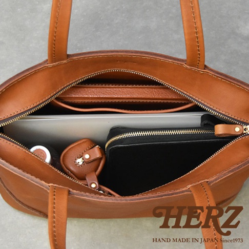HERZ HAND MADE IN JAPAN Since1973 的經典棕色皮革托特包，內部整齊收納了平板電腦、筆記本和化妝包。