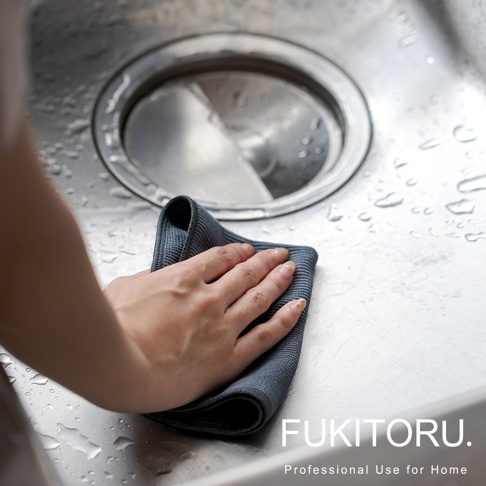 一隻手正用深灰色超細纖維擦拭布擦拭濕漉漉的廚房水槽。