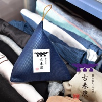 深藍色立體三角形調濕炭包，表面有網格紋理，頂部有金色掛繩，附有標籤，標籤上有「古來炭」字樣及繩結圖案。產品置於衣物堆中。