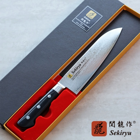 VG10不鏽鋼33層大馬士革三德刀，刀刃呈現獨特紋路，配備黑色手柄，置於黑色包裝盒內的紅色襯墊中。