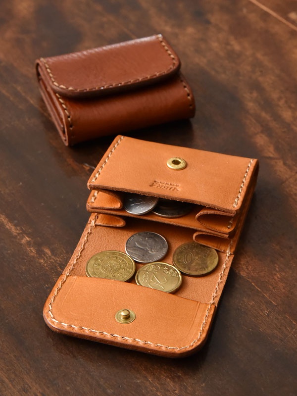 淺棕色牛皮雙折收納零錢包，縫線細緻，附有銅製按扣。其中一個零錢包攤開，展示內部空間及數枚不同面額的硬幣。另一個零錢包則為閉合狀態，呈現其緊湊的造型。