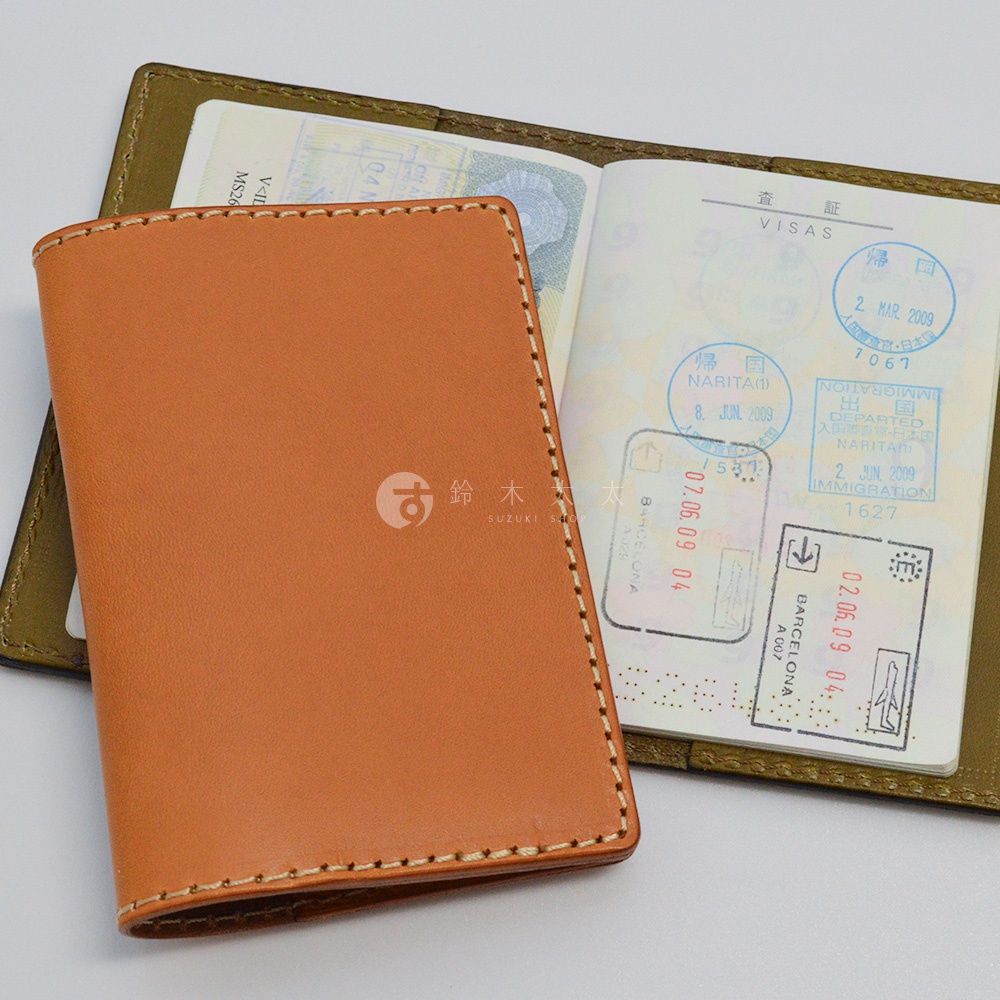 職人手作皮革經典護照套，採用光滑淺棕色皮革，細緻車縫線環繞，內頁夾有一本蓋有日本、西班牙等地出入境章的護照。